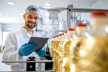 Technologist holding tablet computer and checking production of bottled refined sunflower oil in...