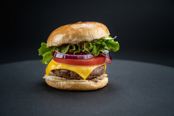 Tasty homemade beef burger with fresh ingredients on dark background, close-up view..