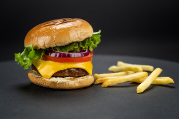 Tasty homemade beef burger with fresh ingredients with french fries on dark background, close-up view..