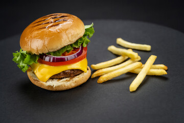 Tasty homemade beef burger with fresh ingredients with french fries on dark background, close-up view..
