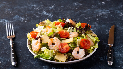 Shrimps salad with fresh vegetables and cheese on a plate served with fork and knife. Healthy and diet food concept