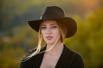 Portrait of a young woman in elegant hat with a wide brim, close up face of beautiful woman outdoor. Cheerful female model. Trendy autumn hat.