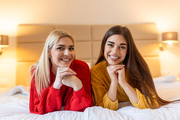 Obraz na płótnie Canvas Happy friends lying on bed at home or hotel bedroom smiling posing looking at camera, lazy weekend leisure activities concept