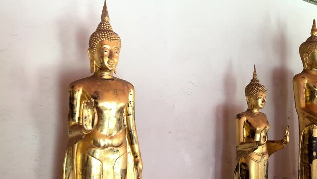 BANGKOK, THAILAND - Circa November, 2021: Golden buddha statues with abhaya mudra gesture at Wat Pho, Temple of Reclining Buddha. Row of standing gilded buddha images  - tracking shot