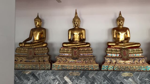 BANGKOK, THAILAND - Circa November, 2021: Golden buddha statues with bhumisparsa mudra gesture at Wat Pho, Temple of Reclining Buddha. Row of sitting buddha images on gilded pedestal  - tracking shot