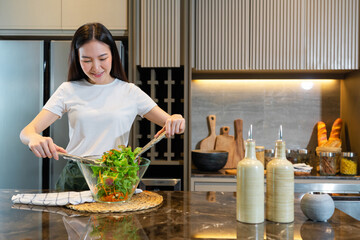 salad concept the woman with white t-shirt and dark green pants standing at the kitchen and making a bowl of green salad