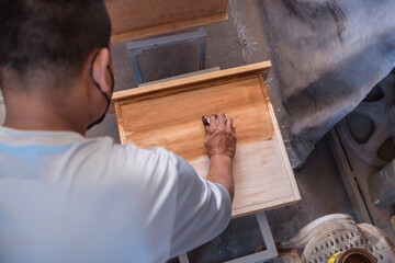 A carpenter applying varnish to a cabinet drawer with a piece of cloth. First coating. At a furniture and woodworking shop.