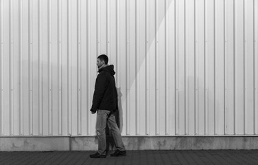 Young caucasian man in casual clothes walking on pedestrian with metal plate background. Black and white photo