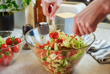 Female hands mixing green vegetable salad in glass bowl at kitchen, Healthy eating and diet concept