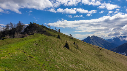 Obraz premium Hiker man at the summit cross of Rosenkogel (Rozca) with scenic view on mountain peaks in the Karawanks, Carinthia, Austria. Border with Slovenia. Triglav National Park. Alps in spring. Goal