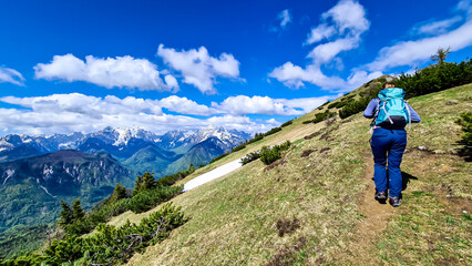 Fototapeta premium Woman hiking to the Frauenkogel (Dovska Baba) with scenic view on the Karawanks, Carinthia, Austria. Borders Austria, Slovenia, Italy. Triglav National Park. Mount Triglav and Mangart in the back. Awe