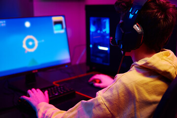 Teenager boy play computer video game in dark room, use neon colored rgb mechanical keyboard, workplace for cybersport gaming, children gaming addiction