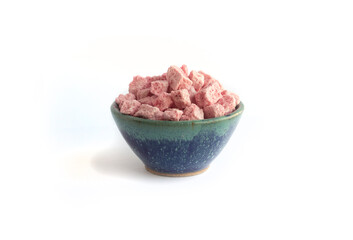 Fototapeta na wymiar Pink Freeze Dried Yogurt or Yoghurt Cubes in Blue Pottery Bowl Isolated on White