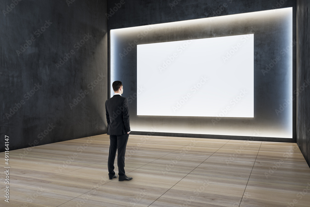 Sticker Man standing in modern exhibition hall interior with illuminated white mock up wall and wooden flooring. Gallery concept.