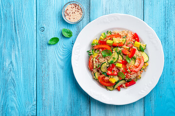 A portion of vitamin, healthy salad with quinoa. avocado, tomatoes and cucumber on a blue background.