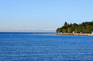 Fototapeta premium Wonderful view of the snow covered Alps mountains against blue Adriatic Sea and sky in winter holidays. Slovenia, Strunjan