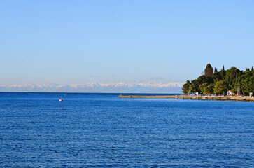 Wonderful view of the snow covered Alps mountains against blue Adriatic Sea and sky in winter holidays. Slovenia, Strunjan