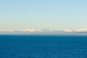 Wonderful view of the snow covered Alps mountains against blue Adriatic Sea and sky in winter holidays. Slovenia, Strunjan