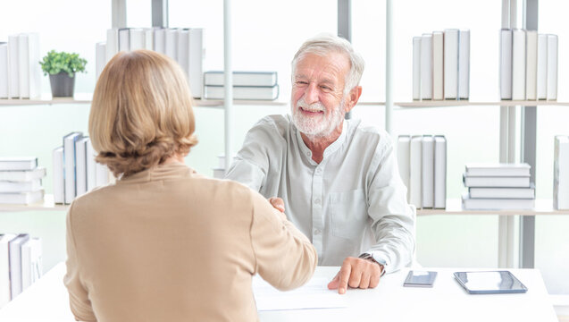 Happy middle aged bank manager sell loan insurance service shake customer hand. Happy older mature businesswoman shaking hand of male partner boss client greeting getting promoted rewarded
