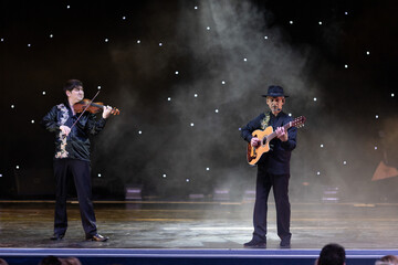 Smoke and light on the stage. Male musicians violinist, guitarist and balalaika player perform a...