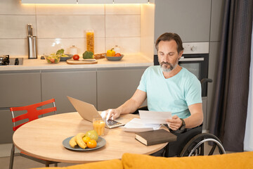 Adult man in a wheelchair working with documents in kitchen