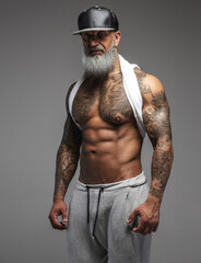 Muscular old man dressed in sportswear against gray background