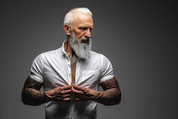 Elderly man with tattooed body posing against gray background