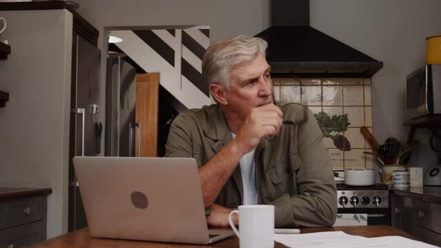 Caucasian mature male working in kitchen on laptop drinking coffee 