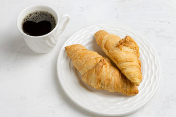 Two delicious croissants on a plate and a cup of black coffee. Morning French breakfast with fresh pastries.