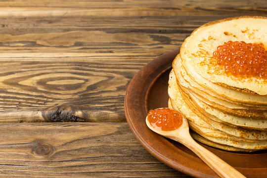 Pancakes for Maslenitsa with red caviar on a plate and a bamboo spoon on a wooden background.