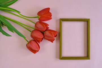 Fresh red tulips and brown wooden frame on pink background. Top view. Close-up. Copy space. Selective focus.