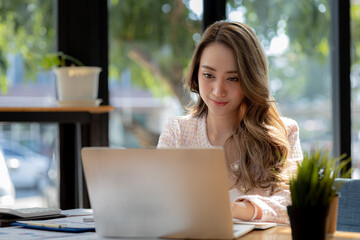 A beautiful Asian businesswoman sitting in her private office, she is checking company financial documents, she is a female executive of a startup company. Concept of financial management.