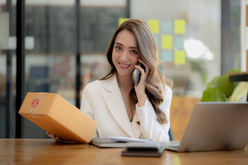 Asian woman is talking on the phone with a customer to confirm an order, she owns an online store, she packs and ships through a private transport company. Online selling and online shopping concepts.