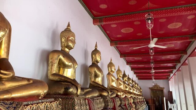 BANGKOK, THAILAND - Circa November, 2021: Golden buddha statues with bhumisparsa mudra gesture at Wat Pho, Temple of Reclining Buddha. Row of golden sitting buddha images on gilded pedestal