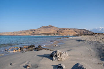 Empty sandy rocky beach in Greece with rough rock. Sea, sun, blue sky background.