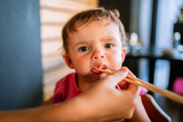 Person feeding a baby girl using chopsticks