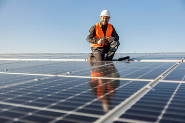 A handyman holding electrical screwdriver and preparing to install solar panels on the roof.