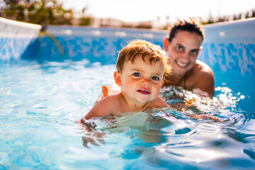 Fototapeta premium Baby learning to swim with his mother in a pool house