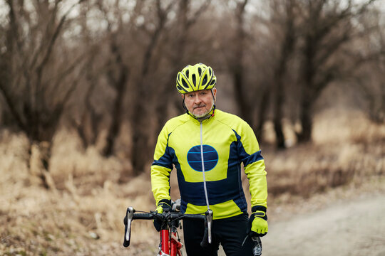 A senior bicyclist standing next to a bike and posing in nature.