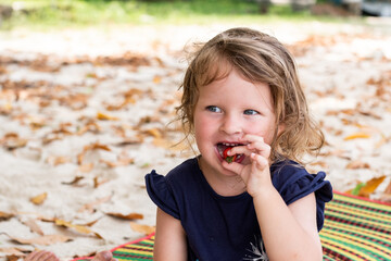 a little curly-haired girl is eating strawberries. funny little girl smiles and eats fruit