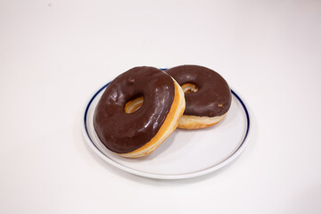 白い背景で撮影された2つの皿に盛られたチョコレートドーナツ