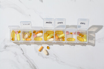 Pills box for daily intake of vitamins and medicines, copy space. Different capsules and tablets in white container.