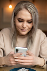 Fototapeta premium Vertical photo of upset tired woman in beige sweater, with manicure, cafe with plate of food, chatting online. Close up