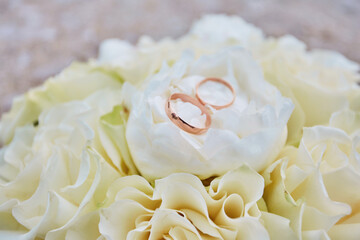 A white wedding bouquet of roses and a pair of wedding rings on it