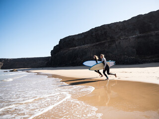 Surfer females on the beach shore running to the waves