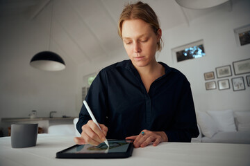 Caucasian female fashion designer working from home designing garments on digital tablet 