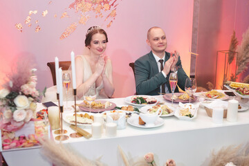 The happy bride and funny groom sit at the table and celebrate the wedding in the banquet hall of the restaurant