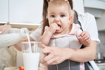 Little girl is sitting in sling and with mother in the kitchen