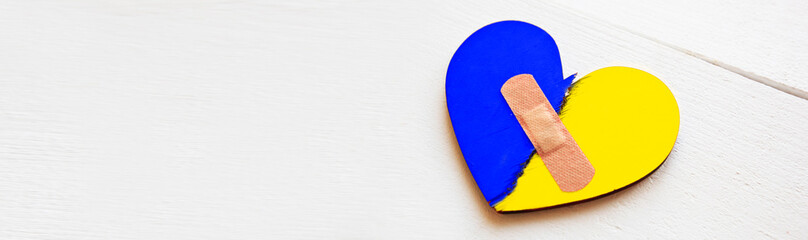 Two parts of broken wooden heart in colors of Ukrainian flag taped by a patch.