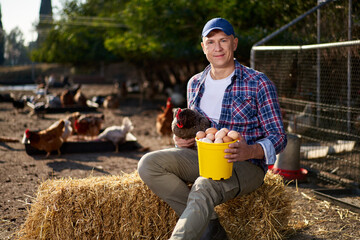 Countryman holding brown chicken in hands in hen house © JENOCHE
